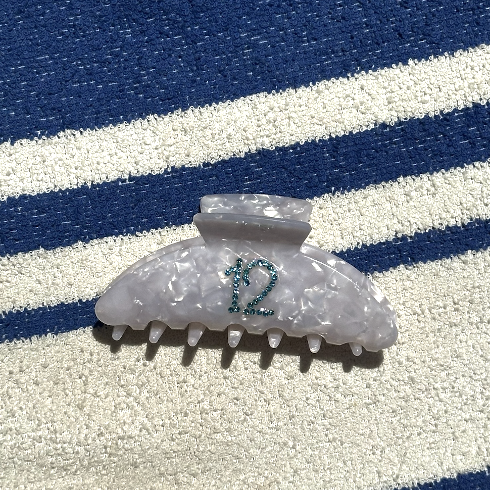 pince a cheveux ecaille blanche en acetate avec strass bleu en forme de 12 sur serviette de plage bleue et blanche
