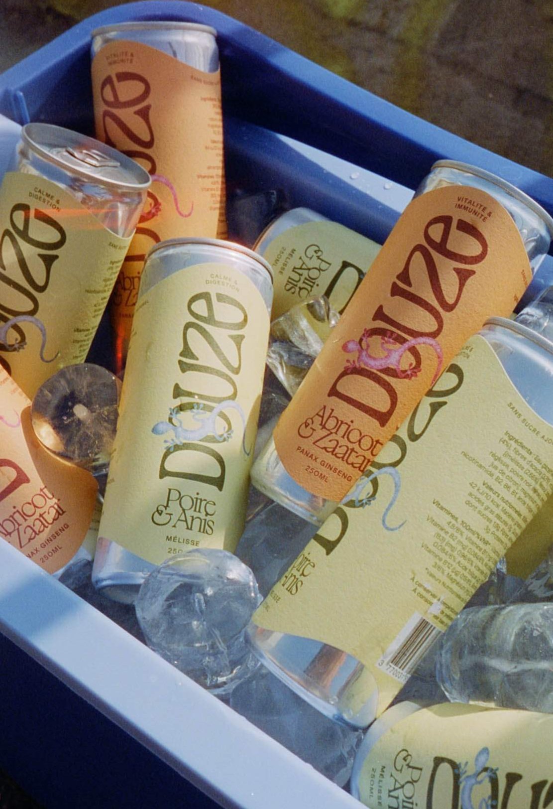 Chilled Douze cans in blue cooler with ice, captured in a nostalgic film photo style with light leak effects.