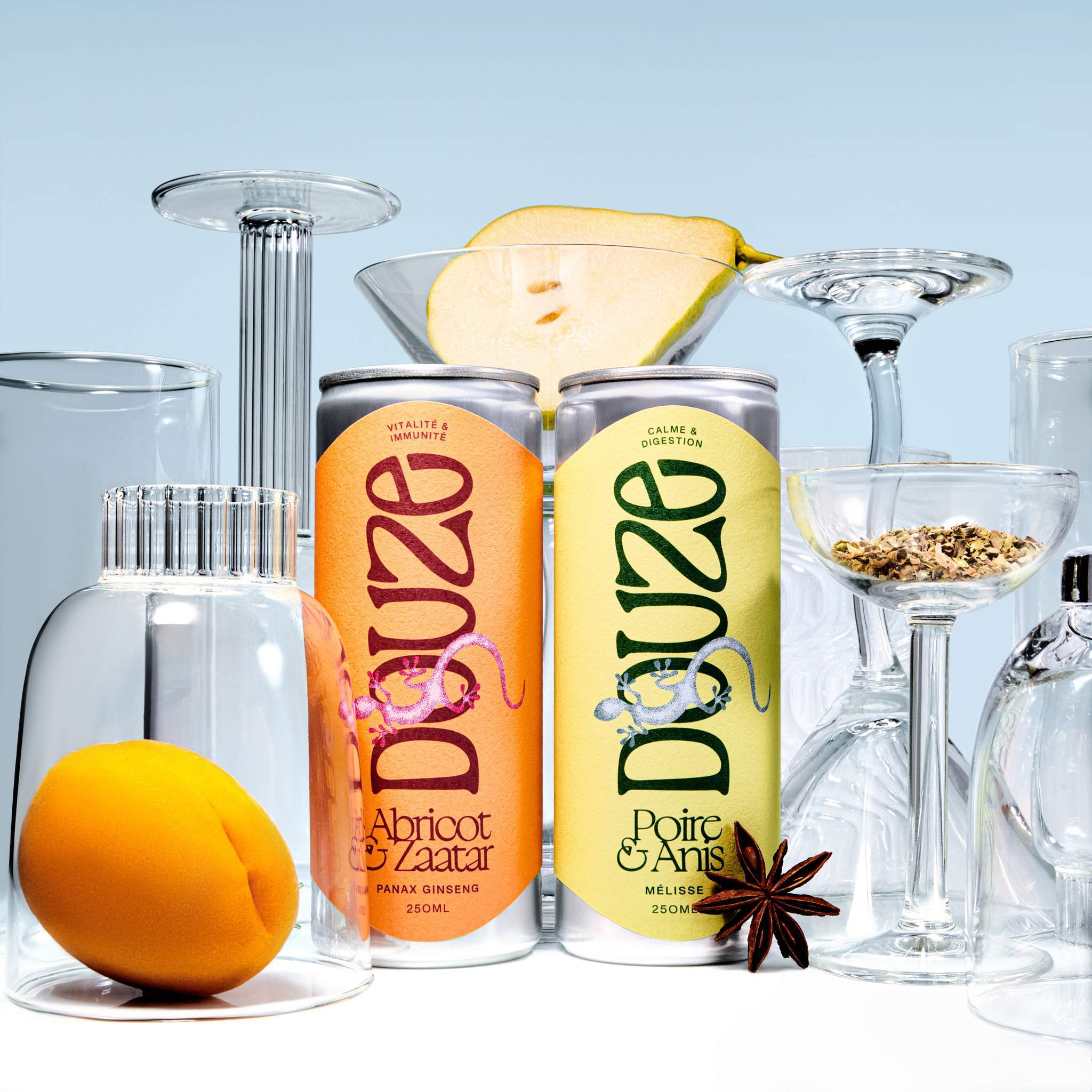 Apricot & Za'atar and Pear & Anise cans among cocktail glasses, whole apricot, sliced pear and spices on blue background.