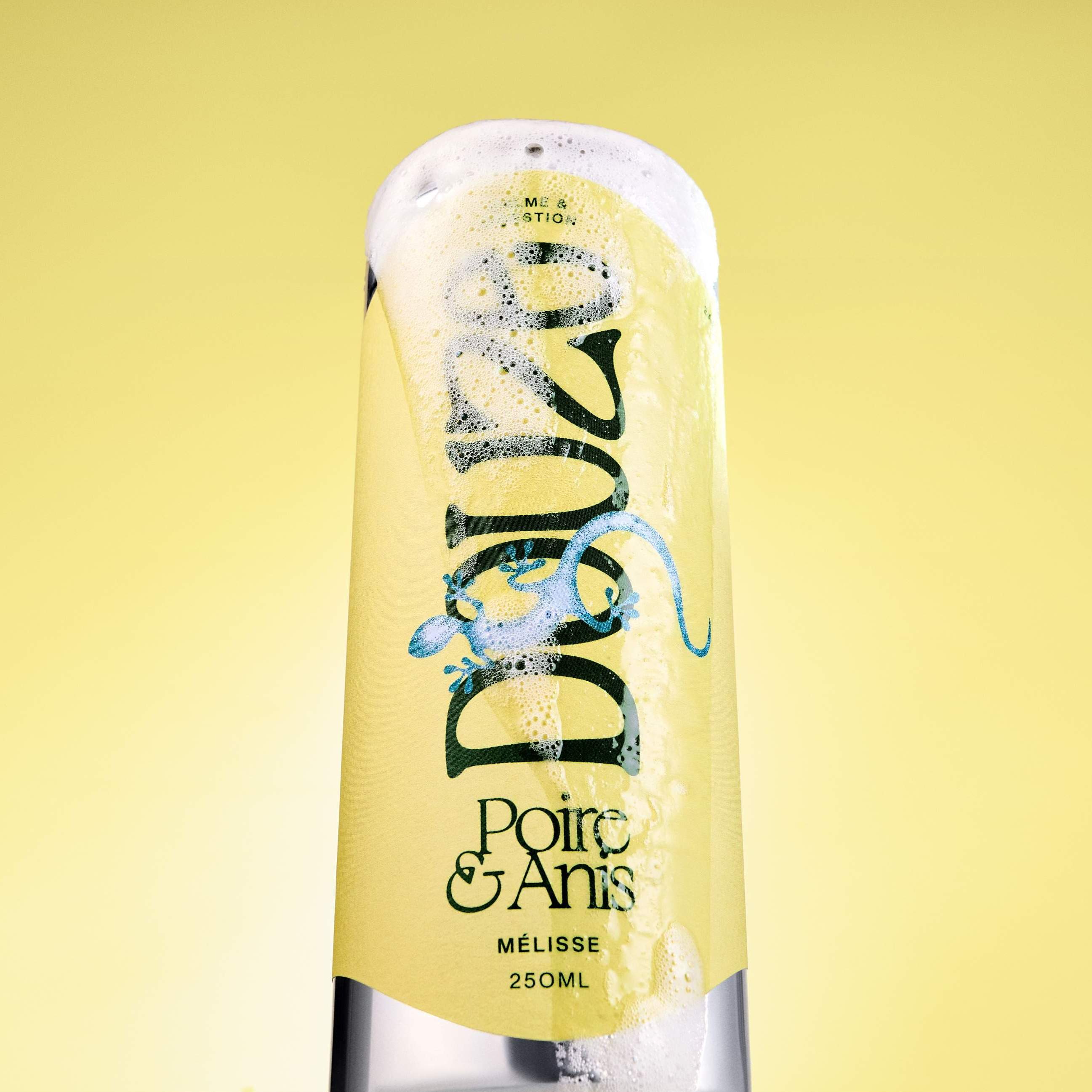 Overflowing Douze Poire & Anise can with frothy bubbles against vibrant yellow background. Image taken from below.