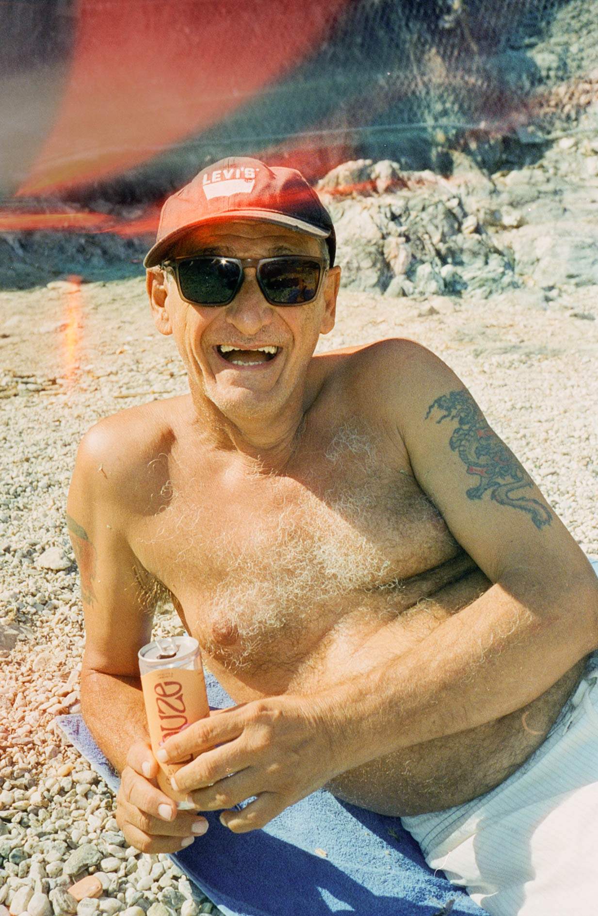 Older man lying on the beach drinking Douze Apricot & Za'atar can