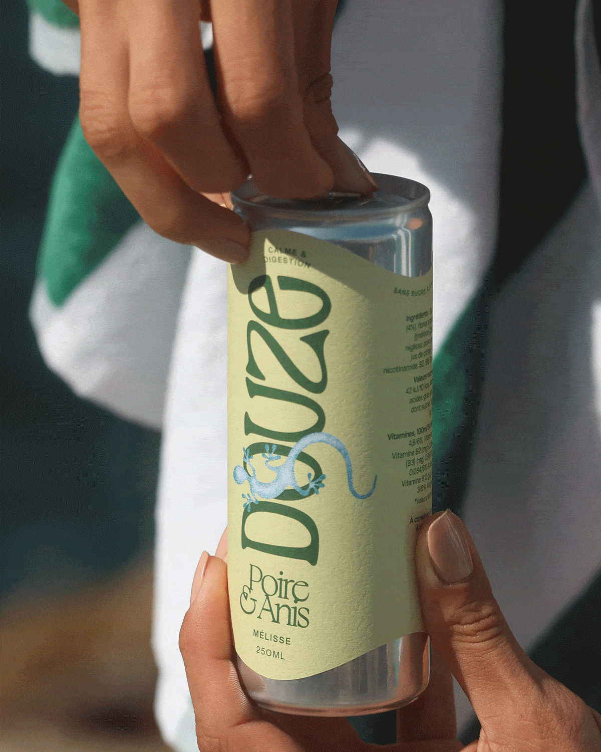 GIF of woman at the beach opening Pear & Anise Douze can, taking a sip in front of coastal background.