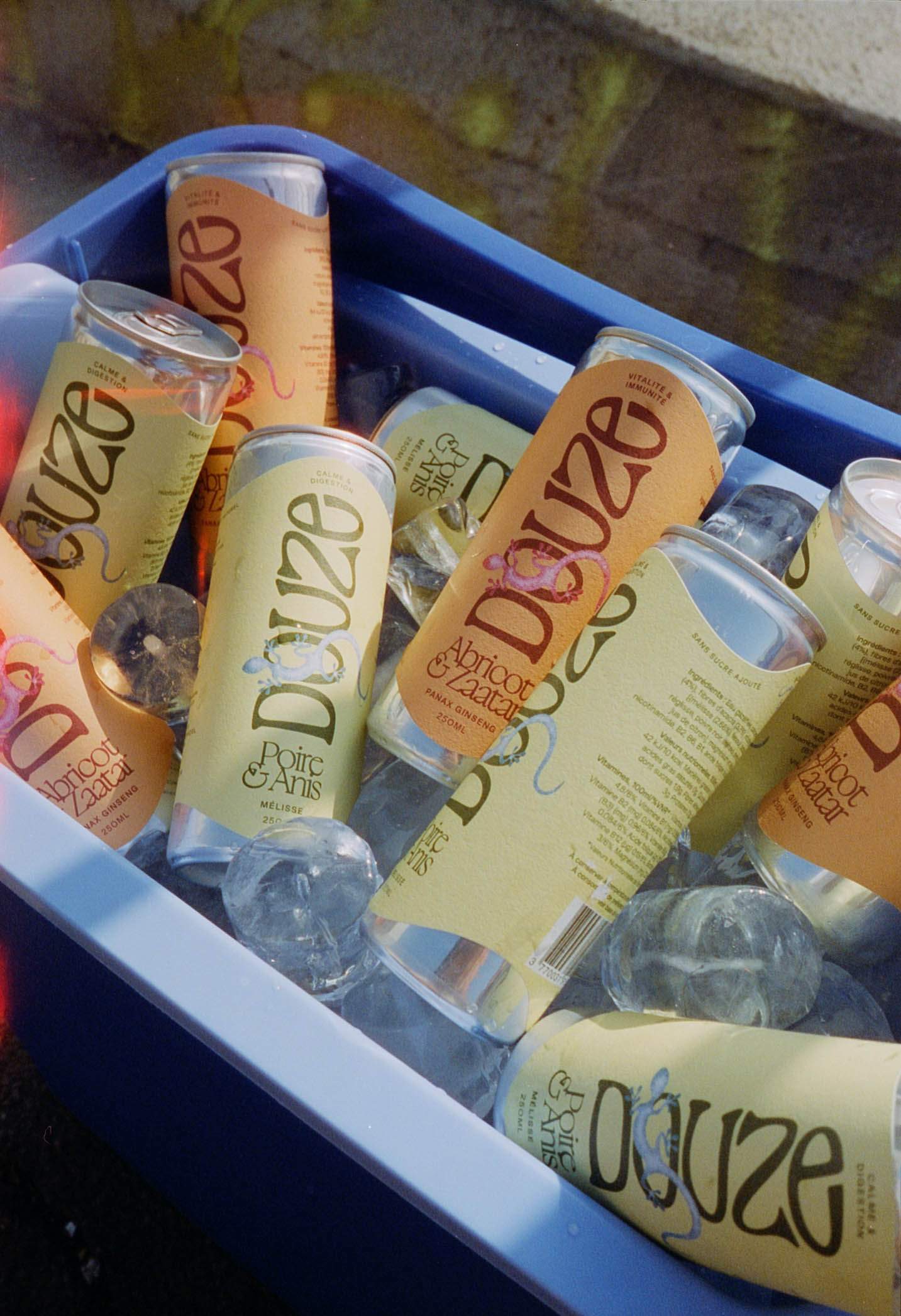 Chilled Douze cans in blue cooler with ice, captured in a nostalgic film photo style with light leak effects.