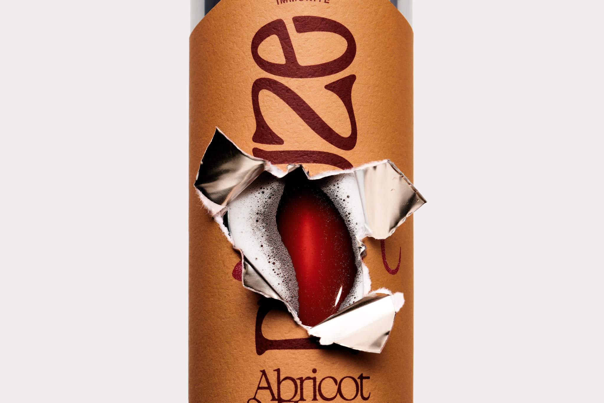 Closeup of a torn and ripped Apricot & Za'atar can label revealing a foamy and sparkling red beverage inside.